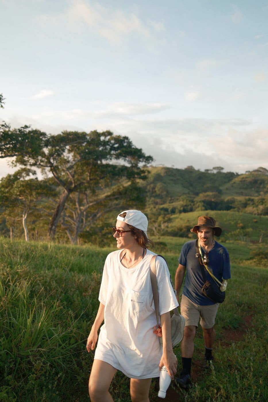 Two residents walking through long grass on the ranch, hills behind them