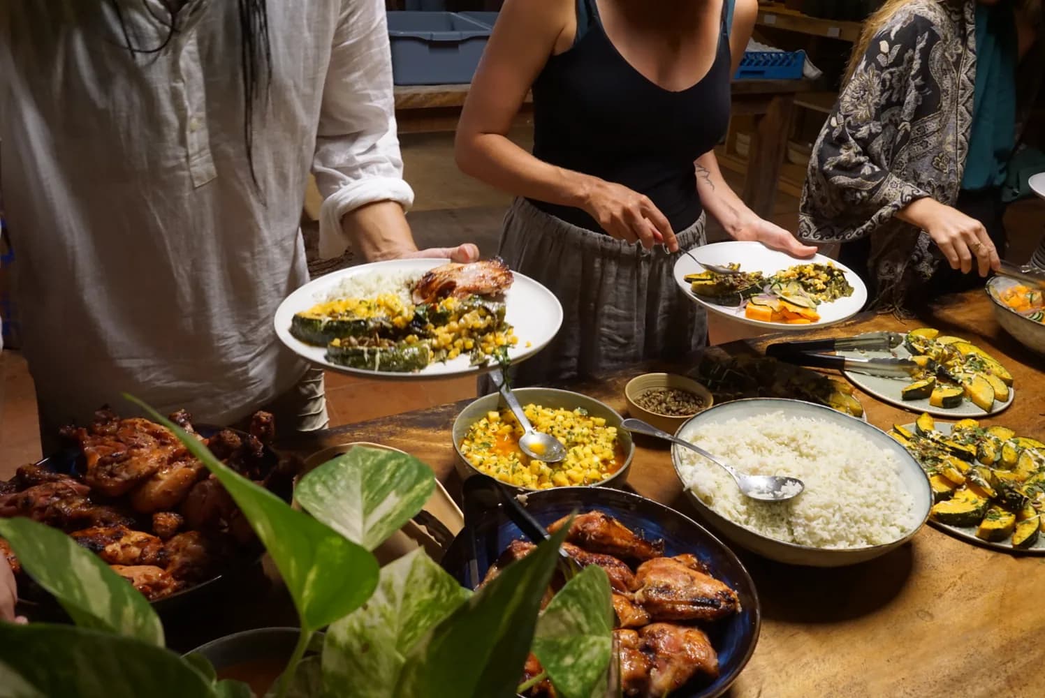 Hands serving from platters of roast chicken, rice and vegetables at a shared dinner table