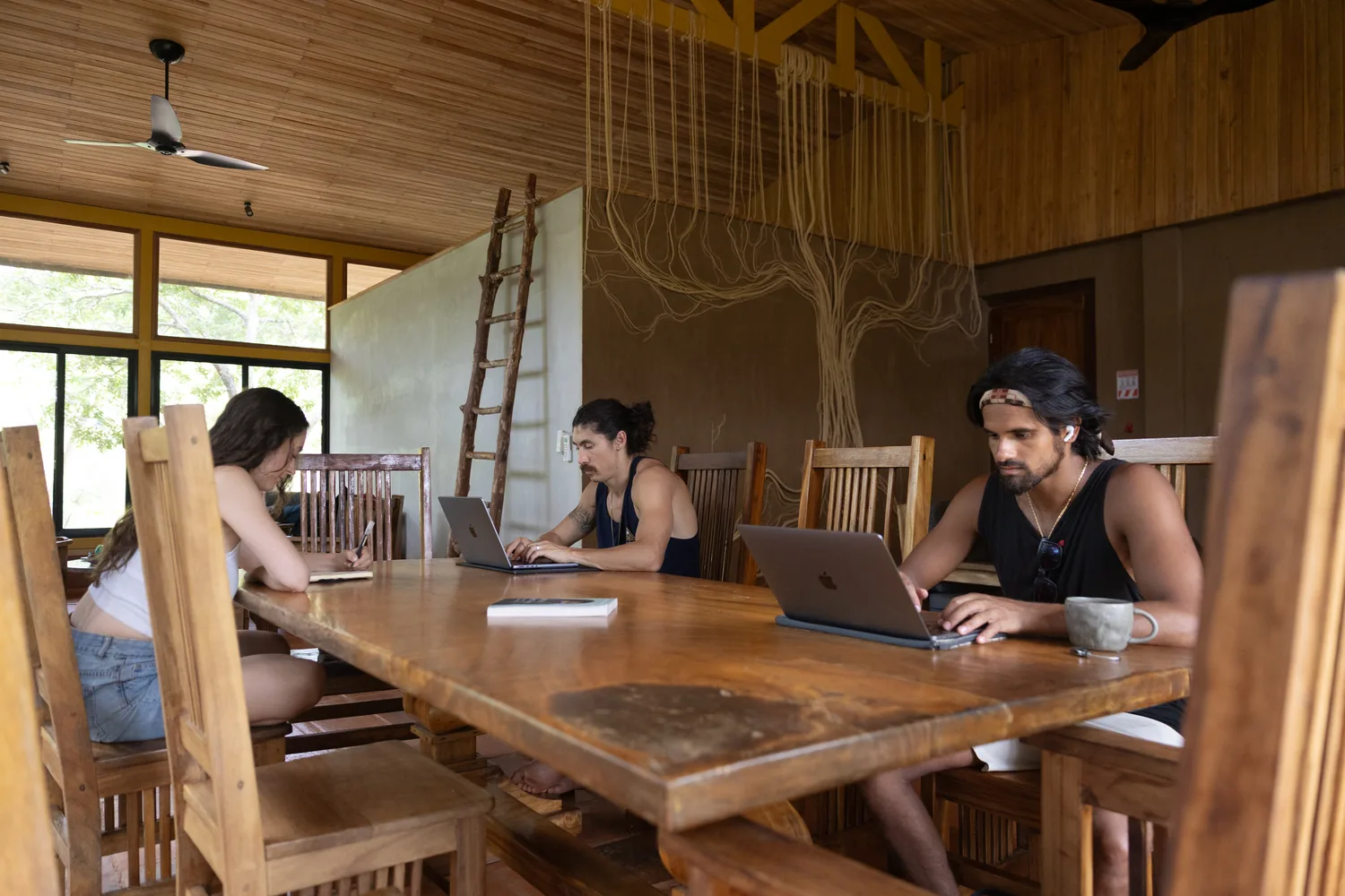 Residents working on laptops around a long wooden table in an open-sided room