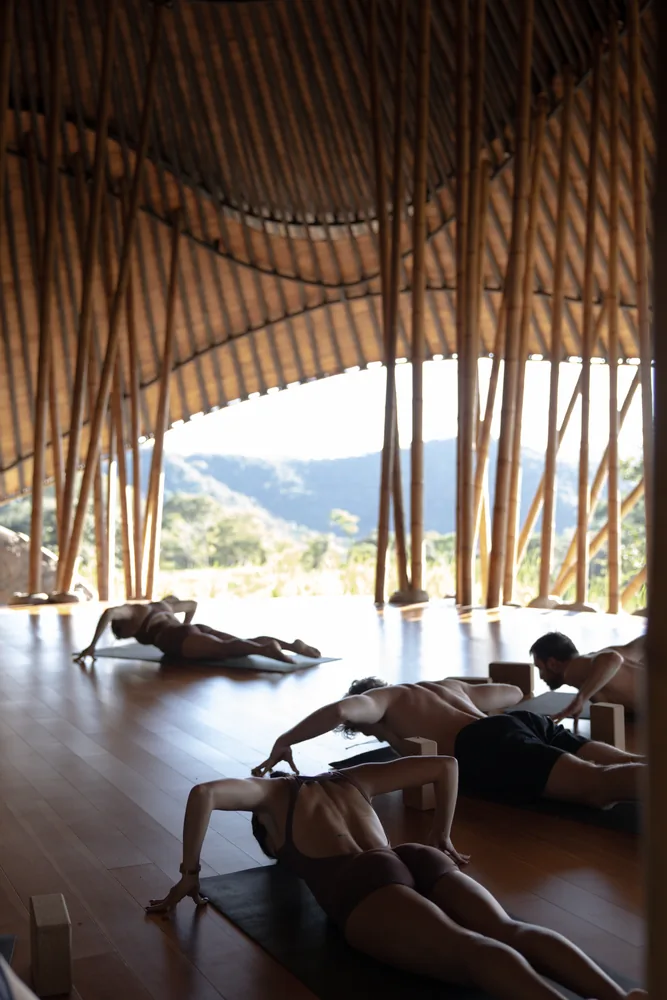 People stretching on mats in the bamboo maloca, open to the hills beyond