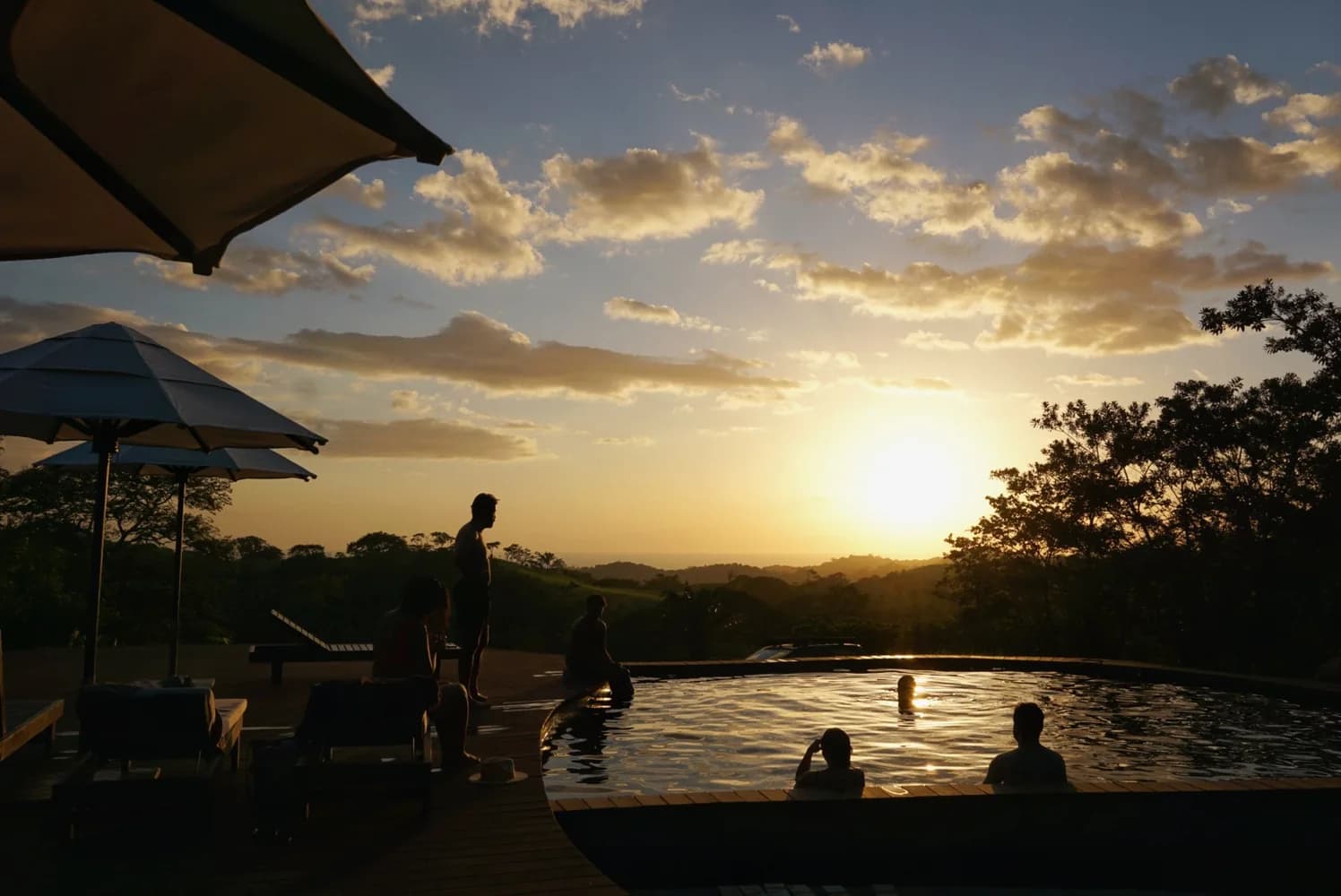 People in and around the pool as the sun sets over the hills
