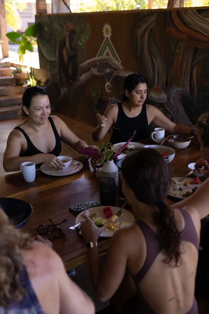 Residents eating together at a long wooden table beneath a painted mural