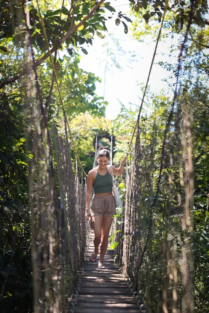 A resident crossing a rope suspension bridge through the forest canopy