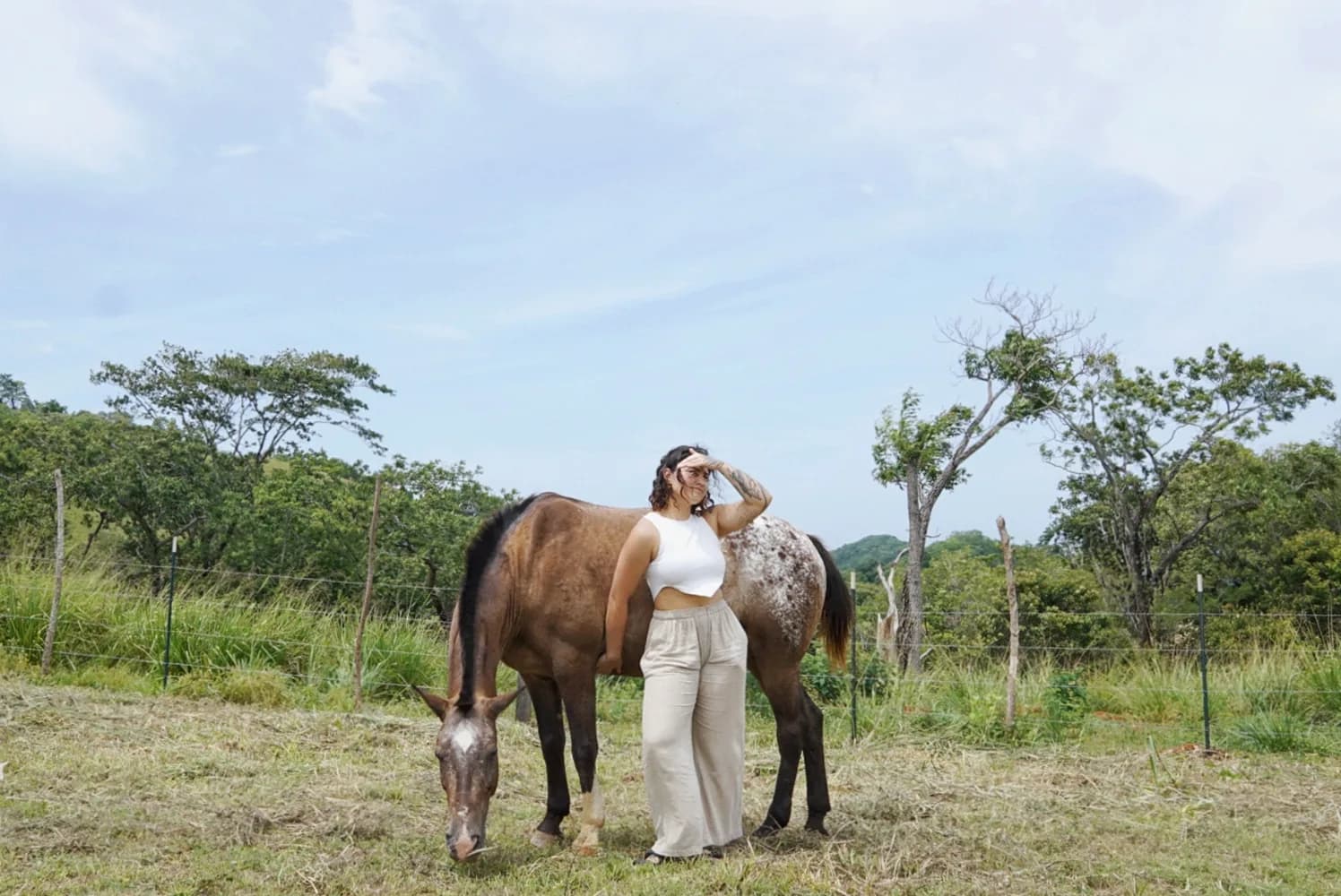 A resident standing quietly beside a grazing horse in a fenced pasture