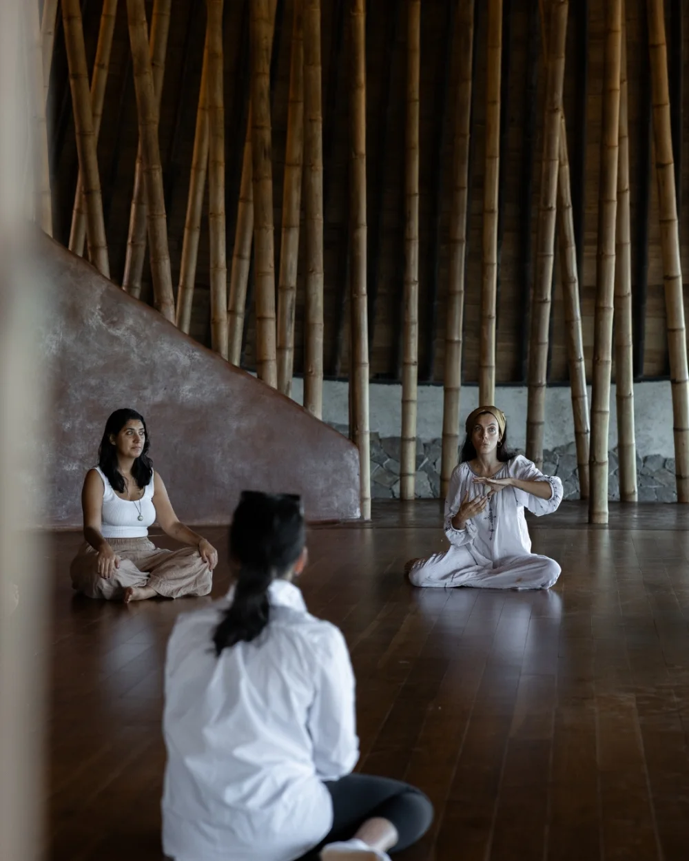 Three people sitting in stillness on the floor of the bamboo studio