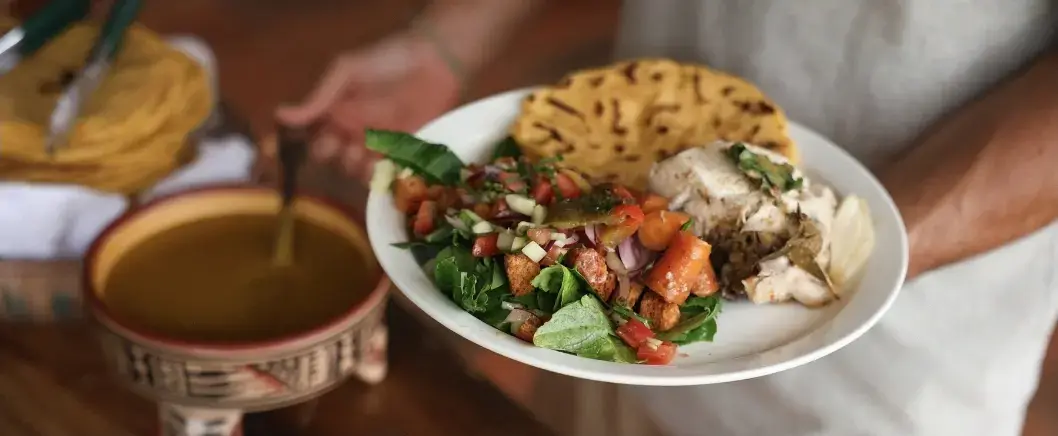 A plate of salad, grilled chicken and a tortilla being served beside a bowl of soup