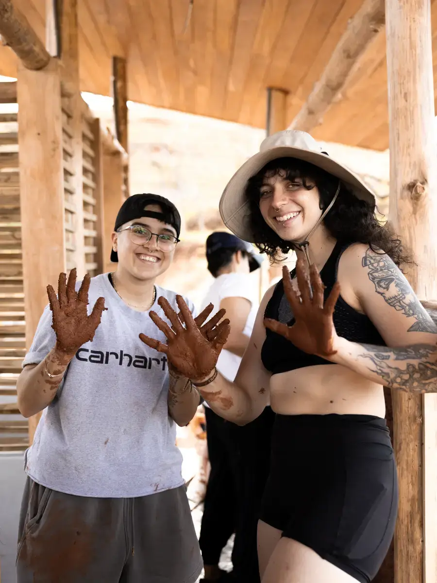 Two people holding up mud-covered hands and grinning