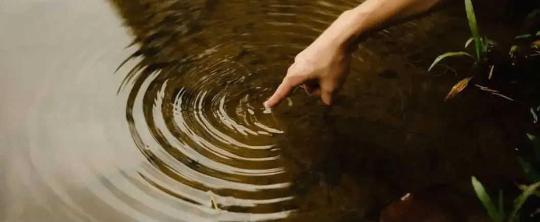 A hand touching the surface of still water, ripples spreading out